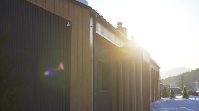Eco hotel building with wooden facade in snowy yard at winter twilight. Modern cabin for guests accommodation at ski resort. Country scene