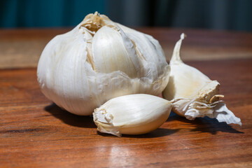 A partially peeled garlic bulb with two cloves rests on a wooden surface, highlighting its natural texture and culinary simplicity.