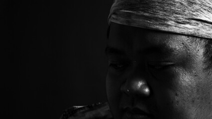 Black and white portrait of a man with headscarf gazing down, symbolizing grief, thoughtfulness, and emotional silence in dramatic tone.