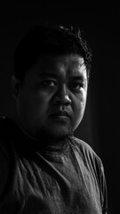 Dramatic low key portrait of a man looking directly at camera, revealing intensity, self-confidence, and focus in high contrast lighting.