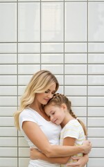Affectionate mother embracing her daughter against a white tiled wall in a loving and tender moment
