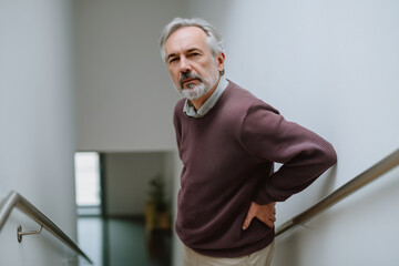 Senior man holding his lower back in pain on staircase
