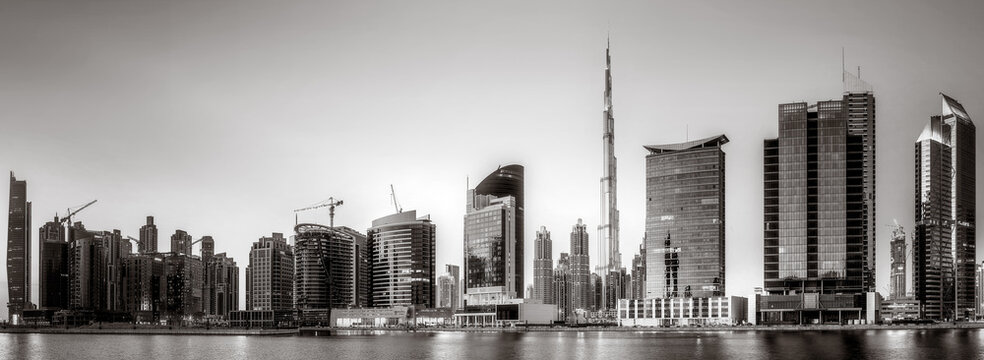 Fototapeta Monochrome city skyline with tall skyscrapers reflecting on calm water under a cloudy sky, Dubai Marina bay UAE