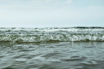 Small, foamy tidal waves reaching the shore, Close up, low angle, water level point of view, cloudy summer day, no people