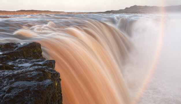 View of the powerful, milky, orange-tinted waterfall plunges over a dark rocky precipice, shrouded in mist and rainbows, a serene majesty, Selfoss, Sveitarf&eacute;lagio &Aacute;rborg, Iceland.