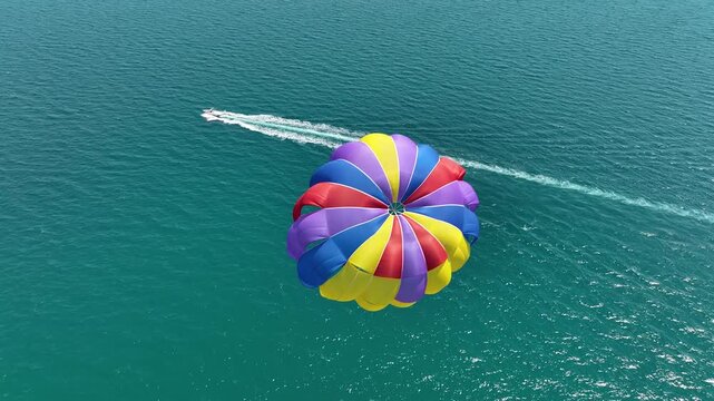 Speedboat pulling a parachute with people moving behind the boat over the water. Aerial view of a speedboat pulling a parachute against a seaside resort. Summer vacation photo.