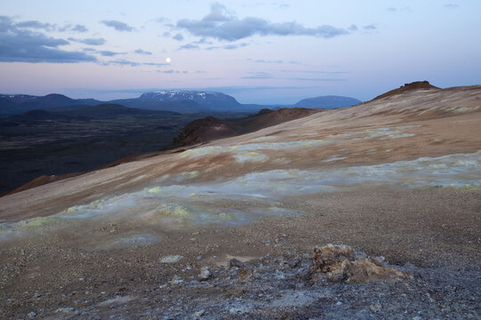 View of barren, otherworldly landscape under a twilight sky with distant snow-capped mountains and volcanic vents, Grindav&iacute;kurbaer, Iceland.