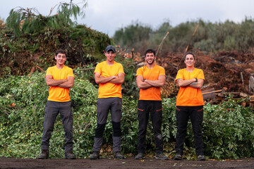 Professional team of smiling gardeners and workers standing among piles of pruned branches and...