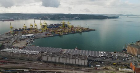 Trieste, Italy - 26 October 2025: Aerial view of the bustling harbor, where colorful shipping containers contrast against the azure sea and industrial cranes.