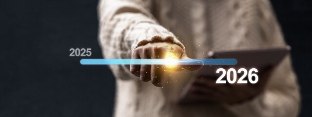 Female hand with tablet slides the loading bar from 2025 to 2026 on a virtual screen. Happy New...