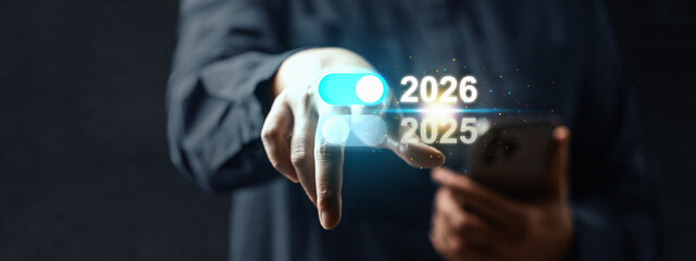 Business hand with cellphone touching the year 2026 above 2025 on a virtual screen. Happy New Year concept or Celebration