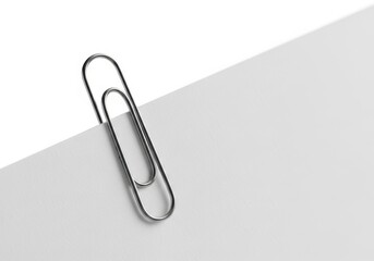 A silver metal paperclip holding a corner of a white sheet of paper, isolated on white background