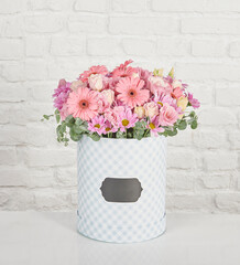 Beautiful floral arrangements: a hand-held bouquet of orange and white roses, and a pink tulip arrangement in a decorative striped box against a white brick wall.