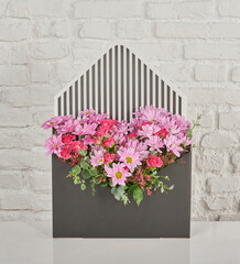 Beautiful floral arrangements: a hand-held bouquet of orange and white roses, and a pink tulip arrangement in a decorative striped box against a white brick wall.