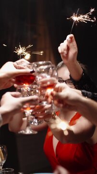 Vertical cinematic slow motion video joyful friends raising glasses with sparklers at festive dinner table cozy warm light holiday atmosphere concept friendship celebration christmas new year