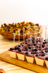 Individual panna cotta desserts with berry sauce and blueberries served in clear cups with spoons, gourmet presentation on wooden table at elegant