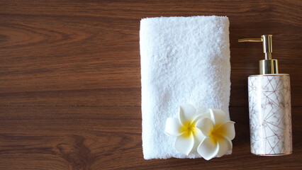 Elegant spa flat lay with white towel, marble soap dispenser, and plumeria flowers on wooden...