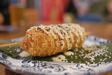 A korean corndog rests on a plate, topped with drizzle and sesame seeds.