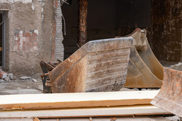Excavator buckets and part of a bulldozer blade, in front of a demolition house wall.