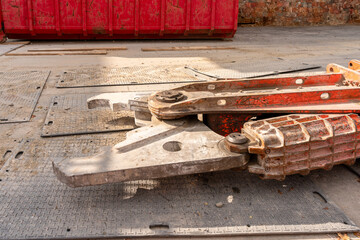 Close up on the jaws of a red concrete crusher on the ground of a construction site. Red rubble container in the background.