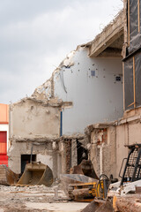 Construction site with demolition house, and construction site equipment, like excavator buckets, and hydraulic excavator accessory lying around.