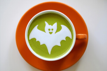 Top view of green tea Matcha Latte in orange ceramic cup with Halloween-themed latte art isolated on white background. This Matcha Latte features a bat halloween ghost design. Generated image