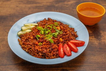 Nasi Goreng – riz frit malaisien aux légumes et protéines, présenté dans une assiette colorée sur table en bois