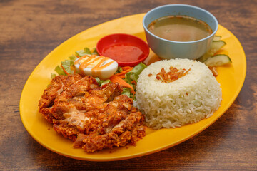 Nasi Lemak – Plat traditionnel malaisien avec poulet mariné frit, riz parfumé au lait de coco, œuf dur et sauce pimentée, présenté sur une assiette colorée sur table en bois. Cuisine malaisienne.