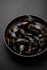 Fresh mussels served in a black bowl on a dark surface for a seafood feast