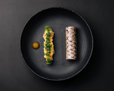 Gourmet sushi dish presented on a black plate with colorful ingredients