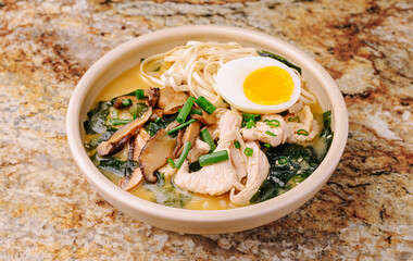 Ramen bowl with chicken, egg, and veggies on a granite counter