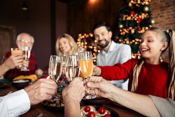 Family Christmas celebration with toasting glasses around a festive dinner in a cozy home interior featuring a decorated tree and warm lights creating a joyful winter mood