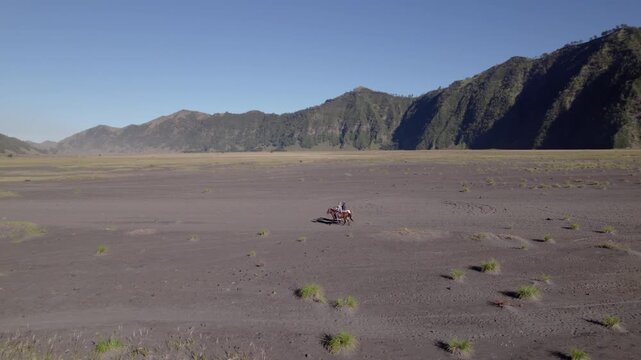 Aerial drone view of two horse riders on lava field near Mount Bromo volcano, East Java, Indonesia, in morning light