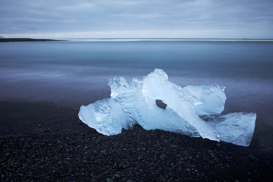 View of glistening ice diamonds scattered on the black sand beach, contrasting against the muted blues of the ocean and sky, Jokulsarlon, Sveitarf&eacute;lagio Hornafjorour, Iceland.