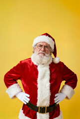 Naklejka premium Santa Claus poses confidently is angry and focused with his hands on his hips against a bright yellow background during the holiday season