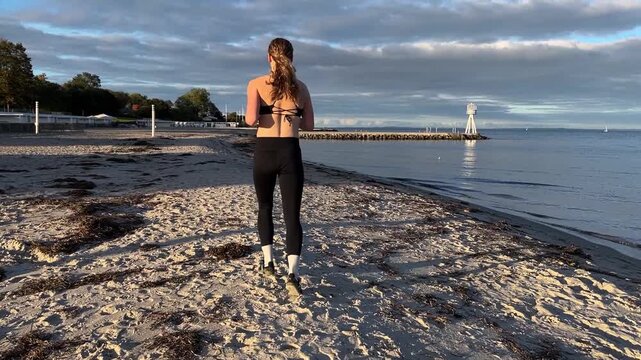 back view of a woman running on the beach at sunset slowmotion