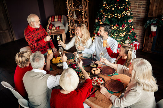 Family gathers around a festive Christmas dinner to toast with champagne by a decorated tree and warm lights creating a cozy home holiday atmosphere