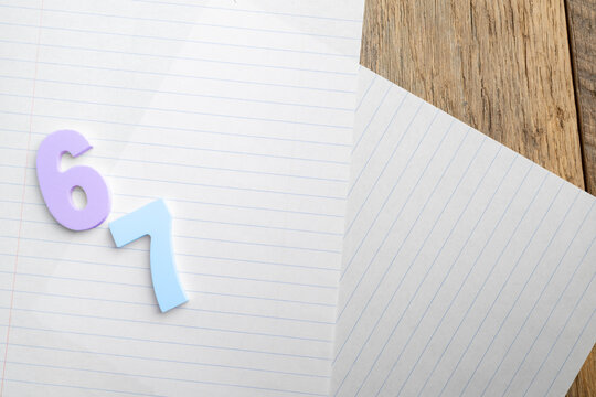 Purple six and blue seven lying on lined notebook paper on a wooden desk depicting the 6-7 trend in schools and social media.
