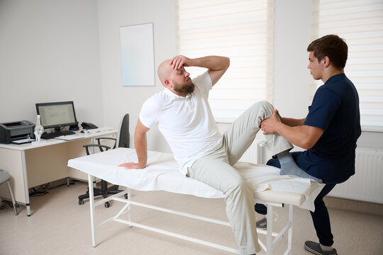 Physiotherapist examining patient knee joint during rehabilitation therapy session in modern medical clinic. Man receiving orthopedic treatment and physical therapy for injury recovery. - Powered by Adobe