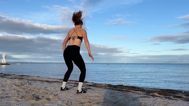 fit young woman exercising outdoor in the sand on the beach doing jumping squat