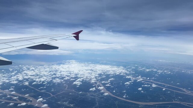 Airplane wing flying over clouds and patchwork landscape