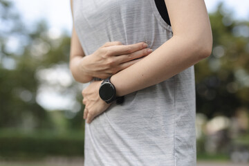Close-up of woman holding stomach in pain while wearing sportswear outdoors, symbolizing abdominal discomfort, cramps or digestive issues. Concept of health problems and fitness concerns.