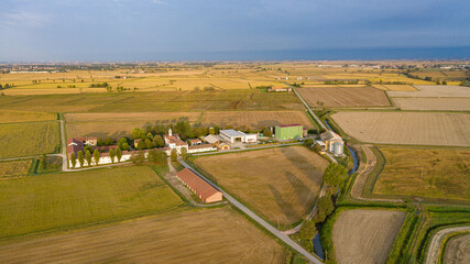 Aerial view of sun-drenched fields and a traditional Italian farmstead, with buildings casting shadows on the golden landscape, Confienza, Lombardia, Italy.