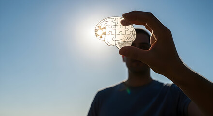 Hand Holding Brain Puzzle Against Sky with Sunburst Representing Mental Solution