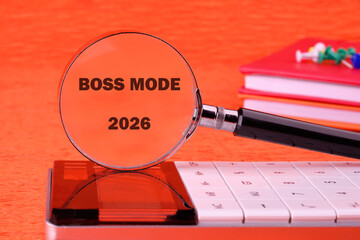A magnifying glass reveals bold text reading Boss Mode 2026, placed on a sleek calculator against a vibrant orange backdrop, showcasing a blend of creativity and ambition