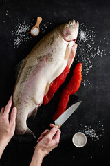 Fresh salmon with fish roe (or red caviar) on black slate background, chef holding a kitchen knife. Cooking process