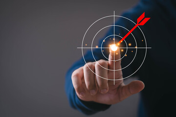 Obraz premium Close-up of a hand touching a digital target with a red arrow hitting the center. Concept of goal setting, success strategy, business planning, achievement, focus, and performance optimization.