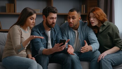 Four multiracial friends at home party looking in mobile phone lost bet casino failure confused sad...