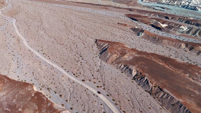 Approaching a red car standing on the road crossing the desert. View on the barren Death Valley National Park, California, USA. From drone.