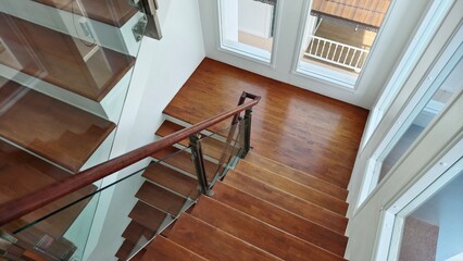 A modern wooden staircase with glass railing in a bright home interior. Clean, elegant design with natural light from large windows. Suitable for interior design, architecture, and home decor concepts